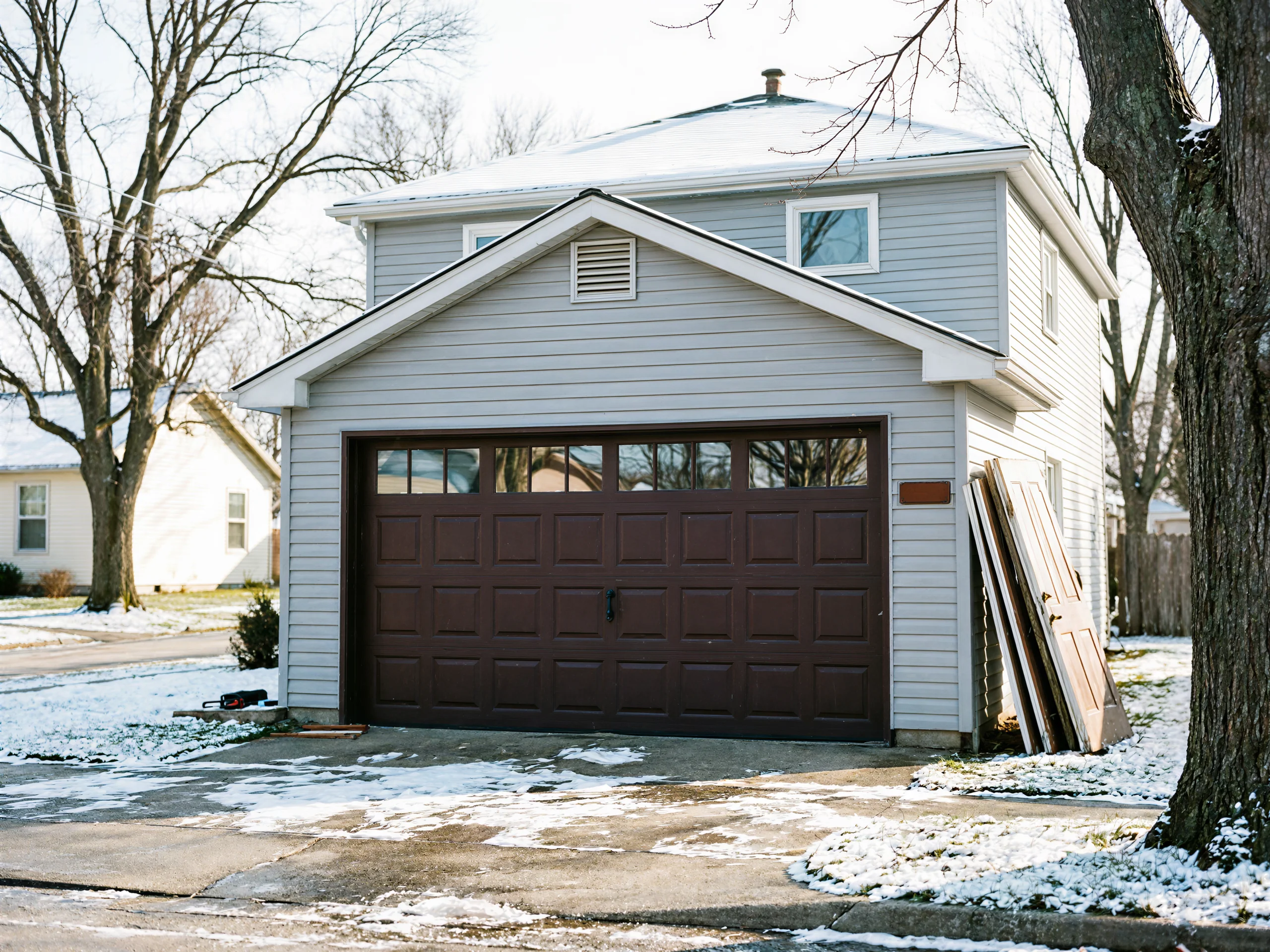 A two-story house with a brown garage door and old doors leaning against the wall.